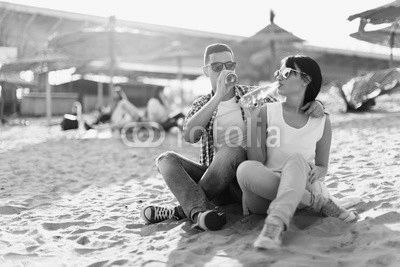 Happy young couple drinking beer and having fun at the beach during sunset