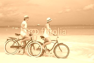 Young happy couple riding bikes on white tropical beach