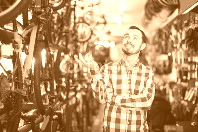 joyous man in bicycle shop chooses for himself sports bike