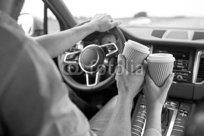 close up of couple driving in car with coffee cups