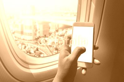 Asian man hand holding blank screen smart-phone on board of airplane near window seat and wing