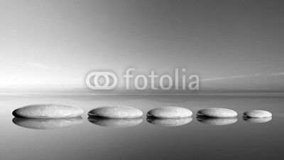 Zen stones row from large to small  in water with blue sky and peaceful landscape background.