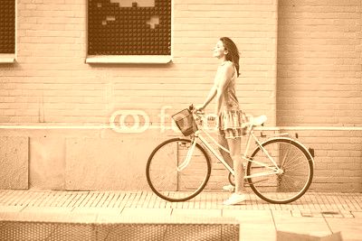 Happy woman with bike standing agains brick building