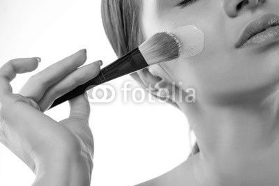 A young woman applied liquid foundation on her face with a brush