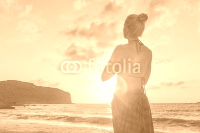 Silhouette of young woman practicing yoga on sandy beach at sunset.