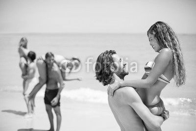 Smiling young man lifting woman at beach