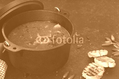 Fish and tomato stew in cast iron pot with grilled bread slices on rustic table