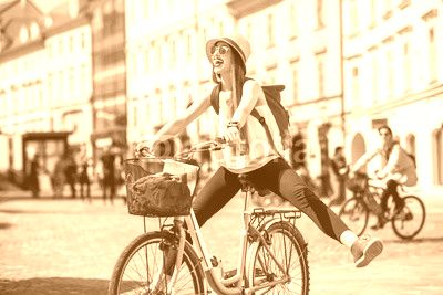 Young female tourist with backpack and hat having fun riding a bicycle in the old city center of Ljubljana in Slovenia