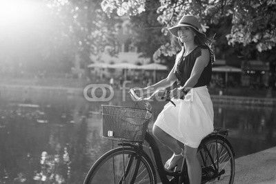 Attractive young woman riding bicycle along a pond in city park
