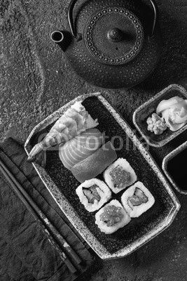 Sushi Set nigiri and sushi rolls in dark ceramic plate with soy sauce, iron teapot and chopsticks over black stone texture background. Top view with space. Japan menu