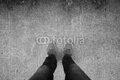 Man with orange shoes standing on a textured, concrete city street.