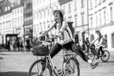 Young female tourist with backpack and hat having fun riding a bicycle in the old city center of Ljubljana in Slovenia