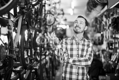 joyous man in bicycle shop chooses for himself sports bike