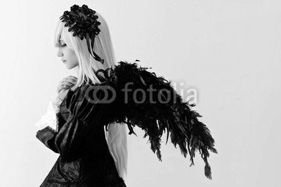 Cosplay girl with white hair , black wings , in a black dress with colored eyes in ryushah and decorations in the studio during the day .