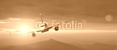 Commercial airplane flying above mountains in sunset