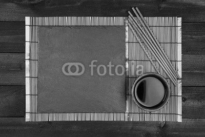 Background for sushi. Bamboo mat and soy sauce on black wooden table. Top view with copy space