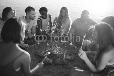 Group of restful friends roasting marshmallows while sitting by bonfire