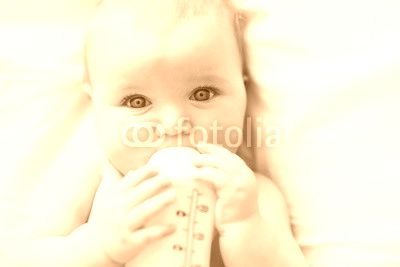 Pretty baby girl drinks water from bottle lying on bed. Child weared diaper in nursery room.