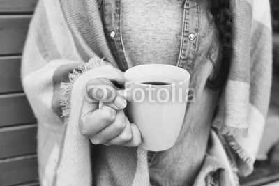Close up view of woman covered in blanket holding cup of coffee. 