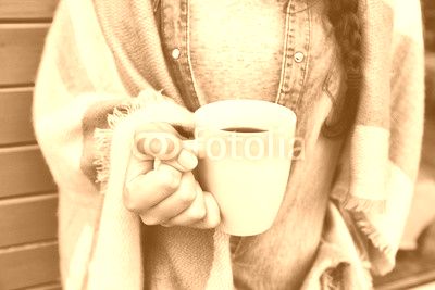 Close up view of woman covered in blanket holding cup of coffee. 