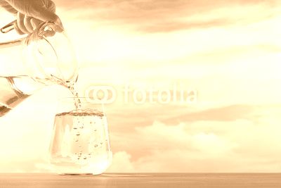 Fresh and clean drinking water being poured from jug into glass on sky background