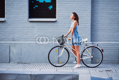 Happy woman with bike standing agains brick building