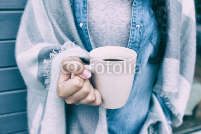 Close up view of woman covered in blanket holding cup of coffee. 