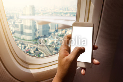 Asian man hand holding blank screen smart-phone on board of airplane near window seat and wing