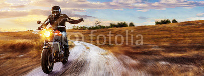 Motorrad fährt auf freier Landstrasse in den Sonnenuntergang