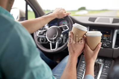 close up of couple driving in car with coffee cups