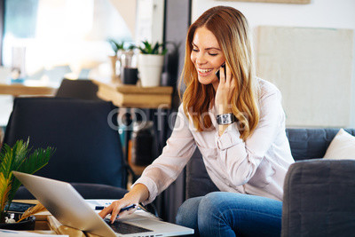 Young woman talking on the phone with a laptop on table in cafe