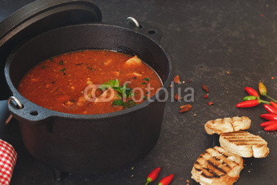Fish and tomato stew in cast iron pot with grilled bread slices on rustic table