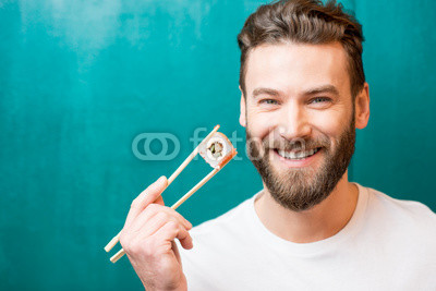 Close-up portrait of a man holding sushi with chopsticks on the green background