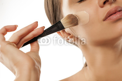 A young woman applied liquid foundation on her face with a brush