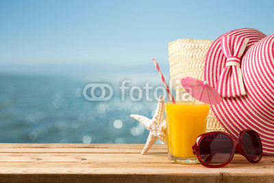 Summer holiday vacation concept with orange juice, hat and sunglasses over sea beach background
