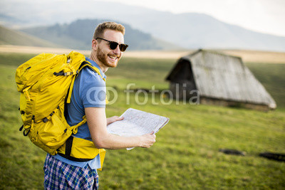 Young redhair man on mountain hiking holding a map