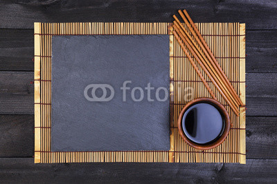 Background for sushi. Bamboo mat and soy sauce on black wooden table. Top view with copy space