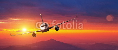 Commercial airplane flying above mountains in sunset