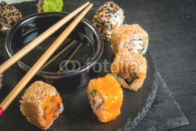 Concept of Japanese food: sticks and sushi, soy sauce and pickled ginger on a black slate stone table. Top view copy space