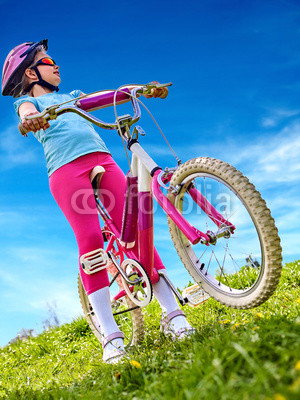 Child traveling bicycle in summer park. Children road bike for running on green grass. Bottom view aganist sky blue. Cycling trip is good for health.