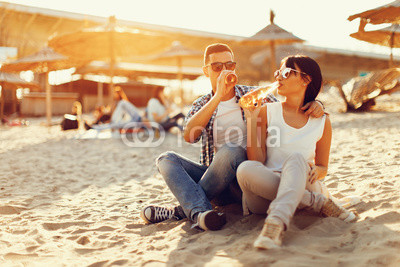 Happy young couple drinking beer and having fun at the beach during sunset