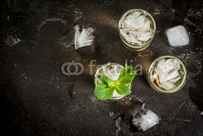 Alcohol cocktail made from golden tequila with ice cubes and mint. On a black concrete table. Copy space top view