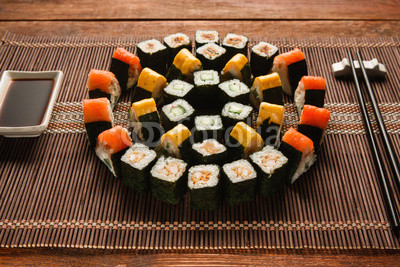 Bright colorful japanese sushi set, round ornament of maki rolls served on brown straw mat, closeup. Japanese food art, national cuisine, restaurant menu photo.