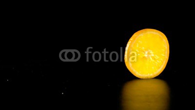 rolling orange fruit slice on black background, slow motion