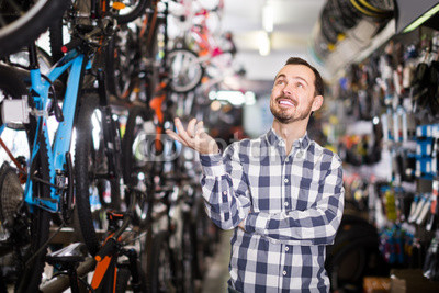 joyous man in bicycle shop chooses for himself sports bike