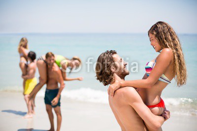 Smiling young man lifting woman at beach