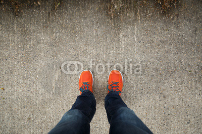 Man with orange shoes standing on a textured, concrete city street.