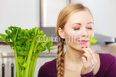 Woman in kitchen holds green celery