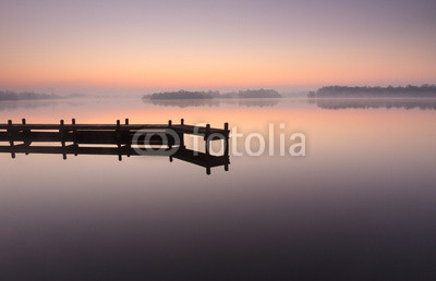 Jetty during a tranquil, foggy dawn at a lake.