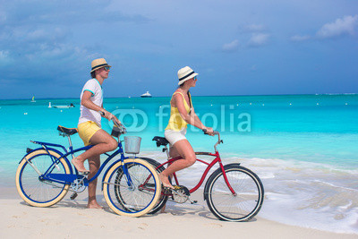 Young happy couple riding bikes on white tropical beach